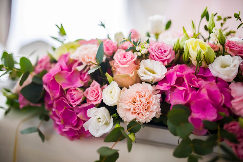 A lush floral arrangement featuring a variety of fresh flowers including pink roses, white lisianthus, light pink carnations, and blush peonies, complemented by green foliage such as eucalyptus leaves