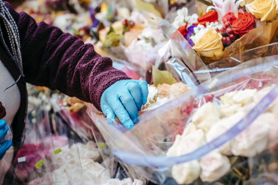 Close-up of a person wearing a purple textured sweater and blue disposable gloves selecting a floral arrangement from multiple clear plastic bags filled with various fresh flowers, including roses in 