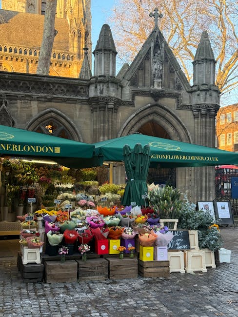 A vibrant outdoor flower stall located in front of a historic stone building with Gothic architectural details, such as pointed arches and ornate carvings, during daylight hours. The stall is covered 