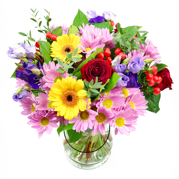 Arranged in a smooth, transparent glass vase and framed by a pristine white background, this mixed bouquet feels like a breath of Maida Vale springtime captured indoors. At its core, deep crimson red roses open in sumptuous layers, their velvety petals creating a rich centre that suggests heartfelt sentiment and timeless elegance. Nestled close by, bright yellow gerbera daisies with dark brown-orange centres glow with upbeat energy, like pockets of sunshine breaking through the canopy of trees along Warwick Avenue. Encircling these focal blooms are generous sprays of soft pink daisies and chrysanthemums, their many slender petals radiating from small yellow eyes, giving the arrangement a plush, comforting fullness and a gentle, almost pastel aura. Threaded throughout, purple and lavender lisianthus introduce cooler tones; their slender, bell-shaped flowers and soft buds add depth and quiet sophistication, as though freshly gathered from a well-kept local garden near Little Venice. Small clusters of polished red hypericum berries punctuate the bouquet, bringing rounded forms and a lively, contemporary twist that contrasts beautifully with the softness of the petals. The flowers are supported by a rich foundation of greenery-broad, dark green leaves lend structure and drama, while lighter, more delicate shoots and sprigs bring movement and a sense of natural growth. Visible through the clear glass, the neatly trimmed stems stand in clean water, evidence of expert care and professional floristry. This arrangement feels warm, joyful, and generous, perfect as a celebratory gift delivered to a Maida Vale flat, a cheerful centrepiece for a small gathering, or a way to bring colour and life into a bright W9 kitchen or sitting room.